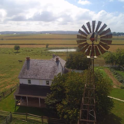 A Scenic Overview Of The Farmhouse And Windmill At Old Windmill Farm, Which Can Be Explored During Their Authentic Farm Tour.